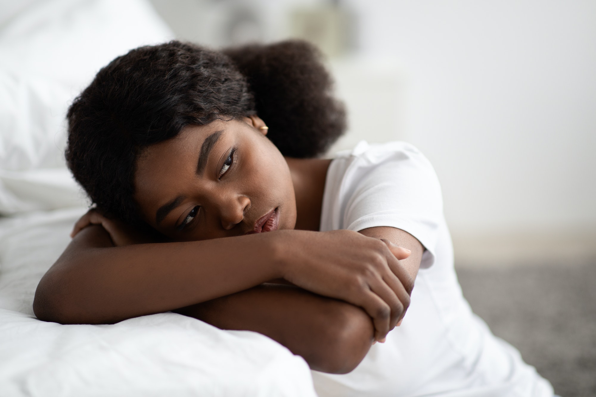 Depressed african american woman sitting by bed at home, closeup